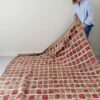 Alfombra vintage marroquí con diseño de cuadros en rojo, beige y marrón, tejida a mano en lana gruesa, colocada sobre suelo claro.