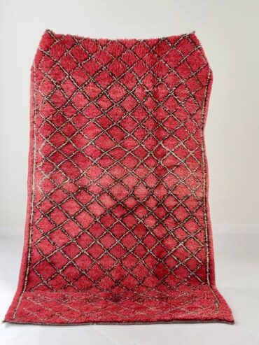 Alfombra bereber vintage en rojo intenso con patrón de rombos en crema y negro, tejida a mano en lana gruesa, sobre suelo claro