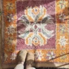 Alfombra vintage bereber pequeña con diseño central floral en tonos granate, naranja y púrpura, tejida a mano en lana gruesa