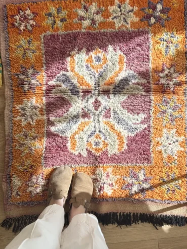 Alfombra vintage bereber pequeña con diseño central floral en tonos granate, naranja y púrpura, tejida a mano en lana gruesa