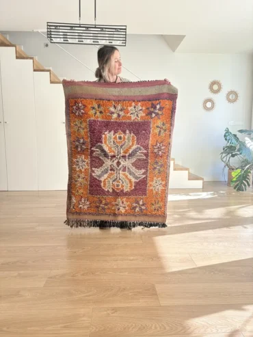 Alfombra vintage bereber pequeña con diseño central floral en tonos granate, naranja y púrpura, tejida a mano en lana gruesa