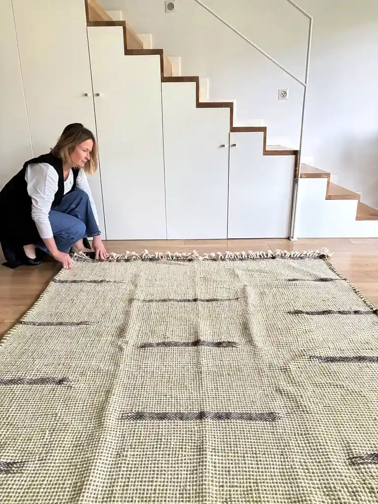 Alfombra kilim verde de lana tejida a mano con franjas negras sobre suelo de madera clara