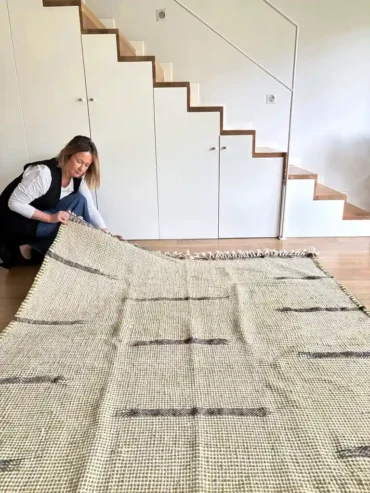 Alfombra kilim verde de lana tejida a mano con franjas negras sobre suelo de madera clara