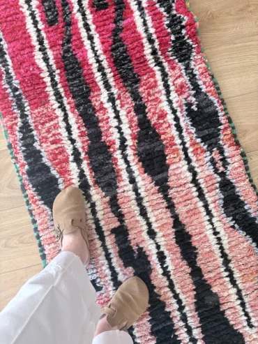 Alfombra bereber Boujaad tejida a mano en lana con fondo rosa y líneas negras. Formato pasillo
