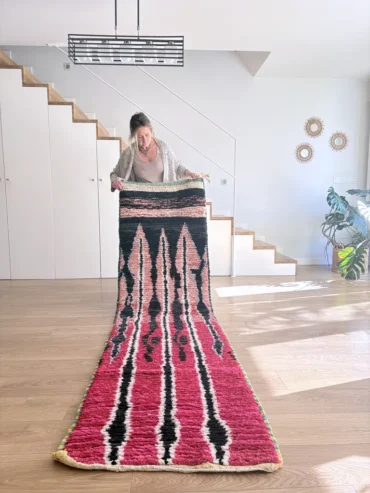Alfombra bereber Boujaad tejida a mano en lana con fondo rosa y líneas negras. Formato pasillo