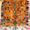 Alfombra bereber de lana con diseño étnico de rombos sobre base naranja, tejida a mano con colores intensos