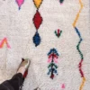 Alfombra azilal de lana Dakota con base clara y motivos en colores vivos distribuidos de forma irregular, tejida a mano en Marruecos.