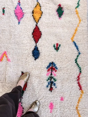 Alfombra azilal de lana Dakota con base clara y motivos en colores vivos distribuidos de forma irregular, tejida a mano en Marruecos.